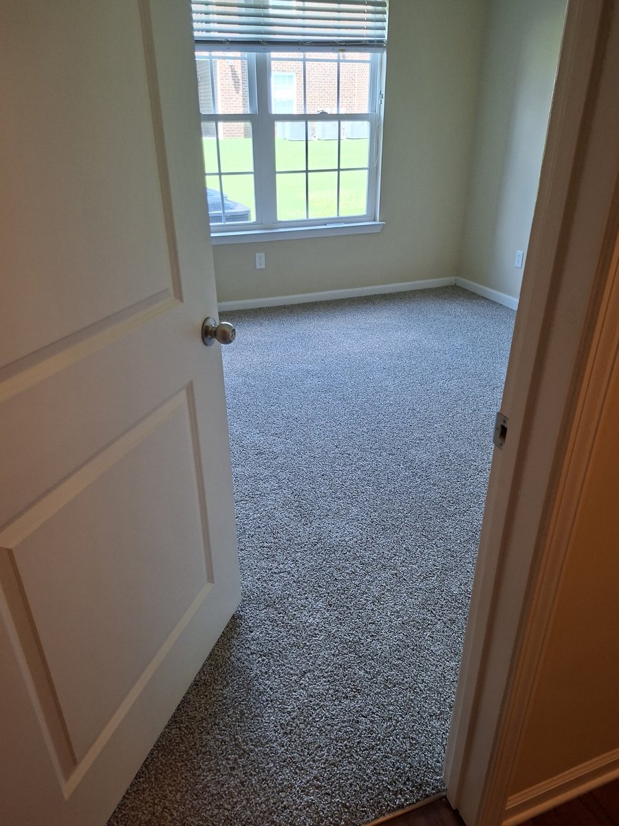 Freshly installed light gray carpet in an empty bedroom, viewed through the open doorway
